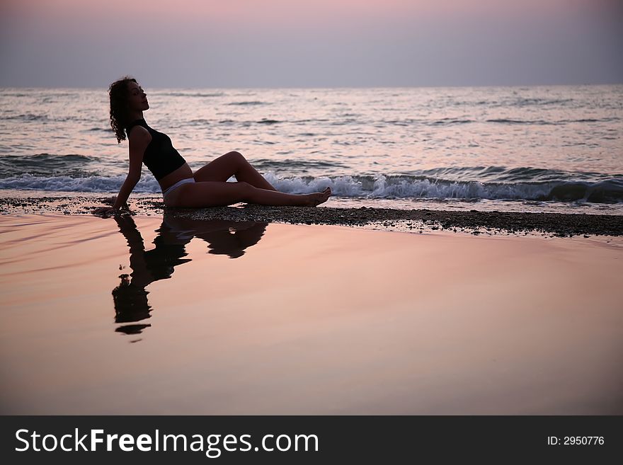 Young woman seats in water on beach on sunset