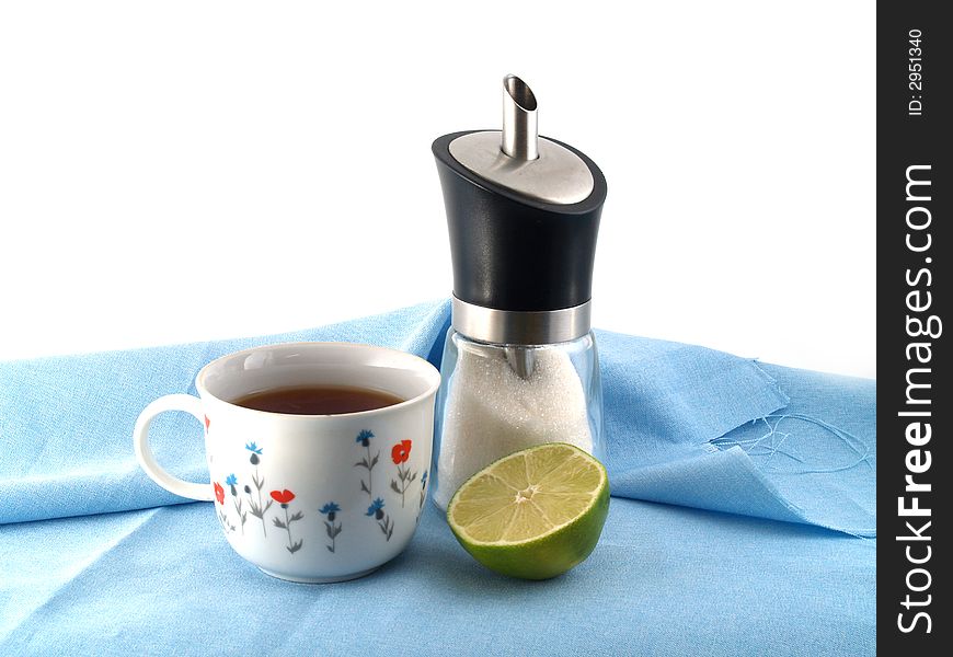 Half of green lime, sugar dispenser and cup of tea