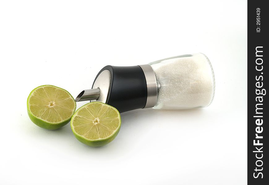 Two halves of green lime and sugar dispenser liyng on the white background