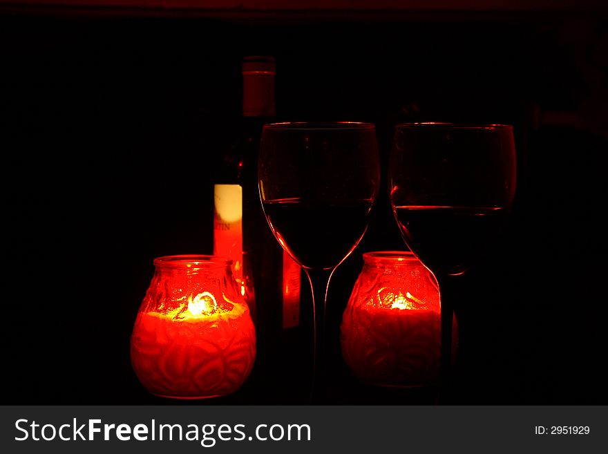 Two glasses with a red wine in an environment of red candles. Two glasses with a red wine in an environment of red candles