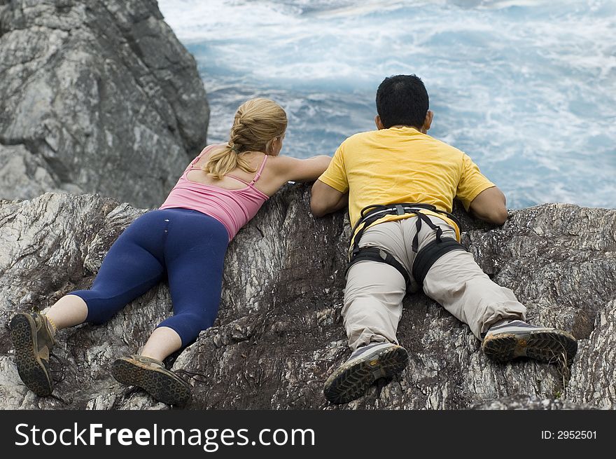 Two rock climbers looking at ocean below a sea cliff