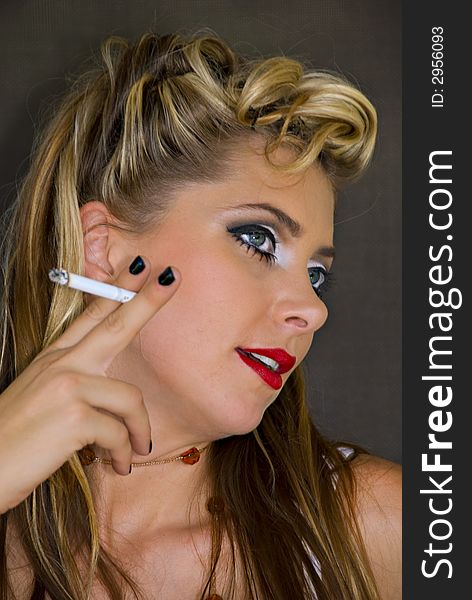 Beautiful young woman in 1950s style makeup and hairstyle holding lit cigarette in right hand. Beautiful young woman in 1950s style makeup and hairstyle holding lit cigarette in right hand