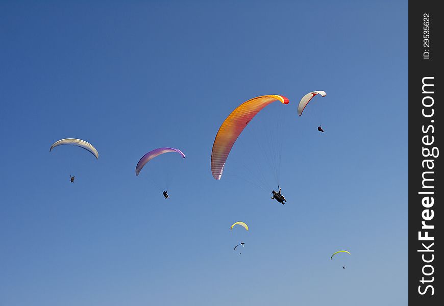 Seven paragliders to slide in clear blue sky. Seven paragliders to slide in clear blue sky