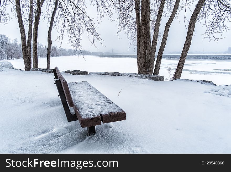 Public bench beside a river on a snowy day. Public bench beside a river on a snowy day