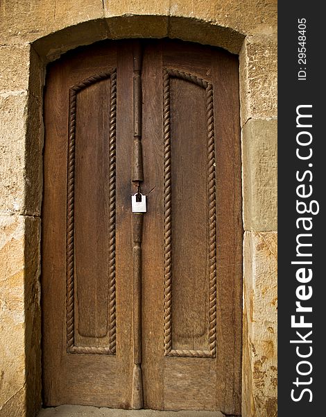 The picture shows a wooden door with panels and a modern padlock. The picture shows a wooden door with panels and a modern padlock.