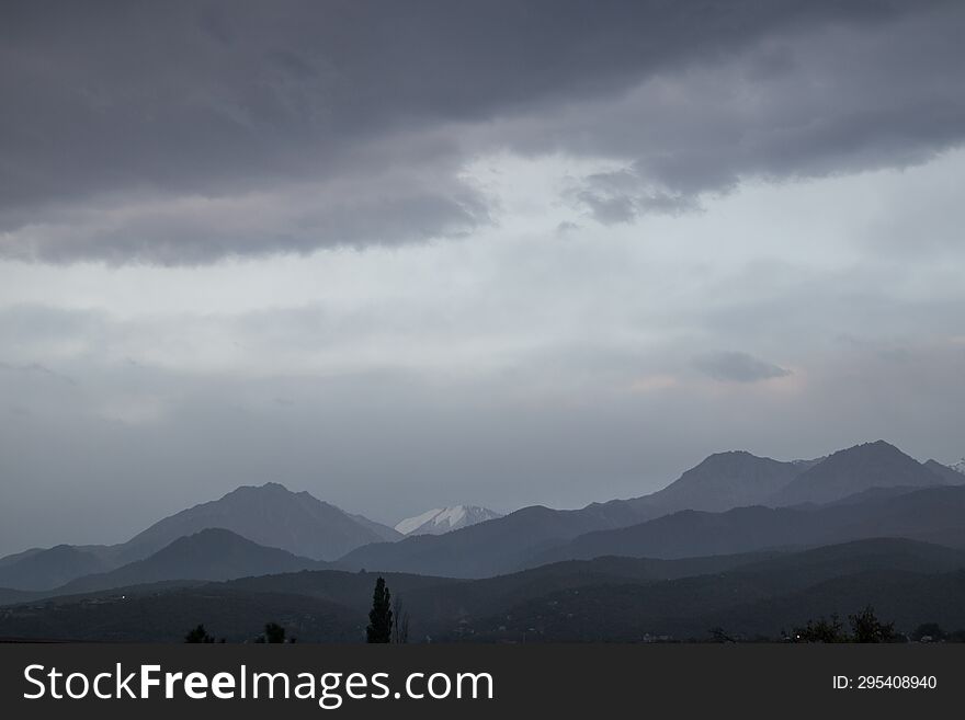 Landscape of the Trans-Ili Alatau mountains on an early cloudy morning in the morning fog with thunderous gray large clouds