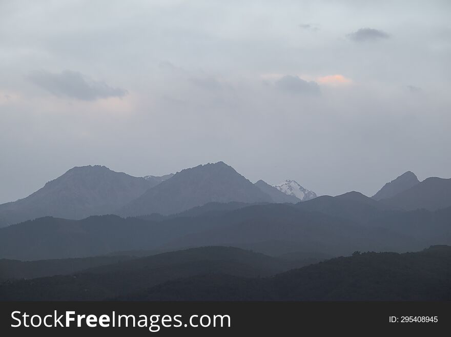 Landscape of the Trans-Ili Alatau mountains on an early cloudy morning in the morning fog