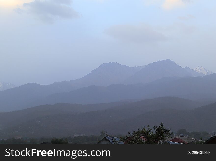 Mountains of Trans-Ili Alatau on an early cloudy morning in the morning fog during sunrise over the suburbs