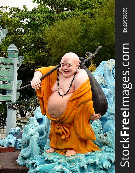 A saffron robed fat laughing Buddhist monk carrying stick and satchel on his travels. Haw Par Villas park, Singapore. A saffron robed fat laughing Buddhist monk carrying stick and satchel on his travels. Haw Par Villas park, Singapore.