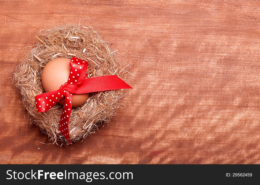 Egg swollen by a red bow lies in the nest on the wooden background