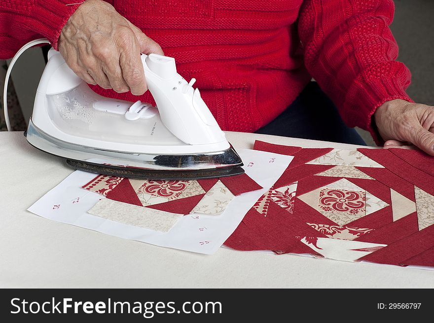 A quilter irons fabric for use in a red and white pieced paper foundation. A quilter irons fabric for use in a red and white pieced paper foundation
