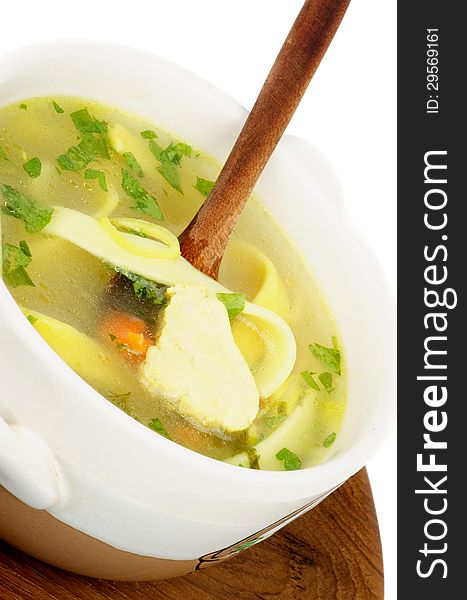 Chicken Noodle Soup with Parsley and Carrot in White Bowl with Wooden Spoon on Wooden Plate closeup on white background
