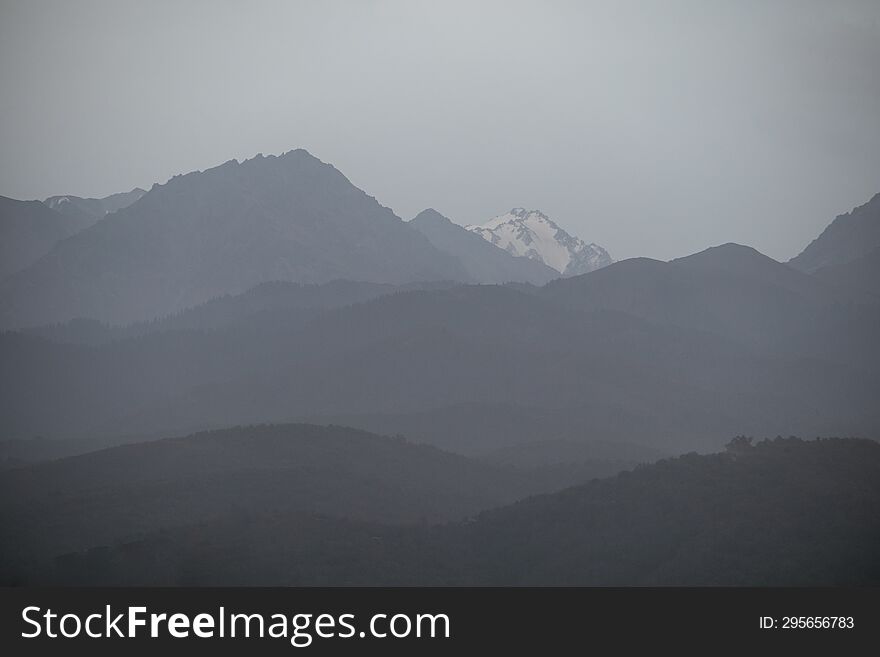 Landscape of the Trans-Ili Alatau mountains on an early cloudy morning in thick morning fog, haze