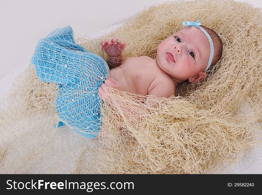 Cute baby girl in net l moves up her knitted blue tail. Cute baby girl in net l moves up her knitted blue tail