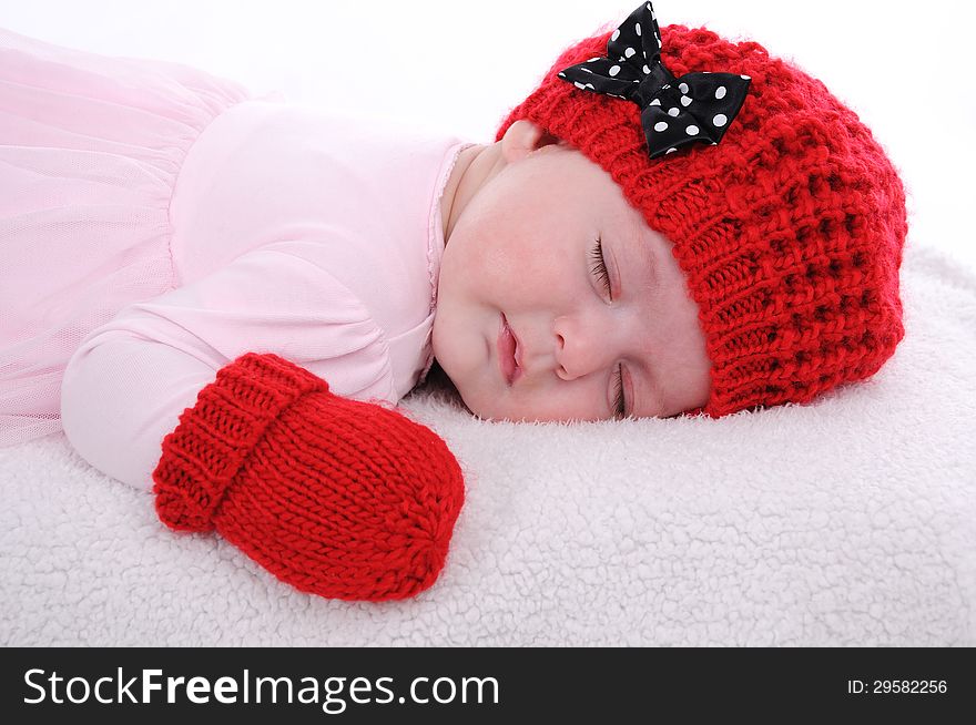 Baby girl dressed in pink dress with red hat and mittens is sleeping. Baby girl dressed in pink dress with red hat and mittens is sleeping