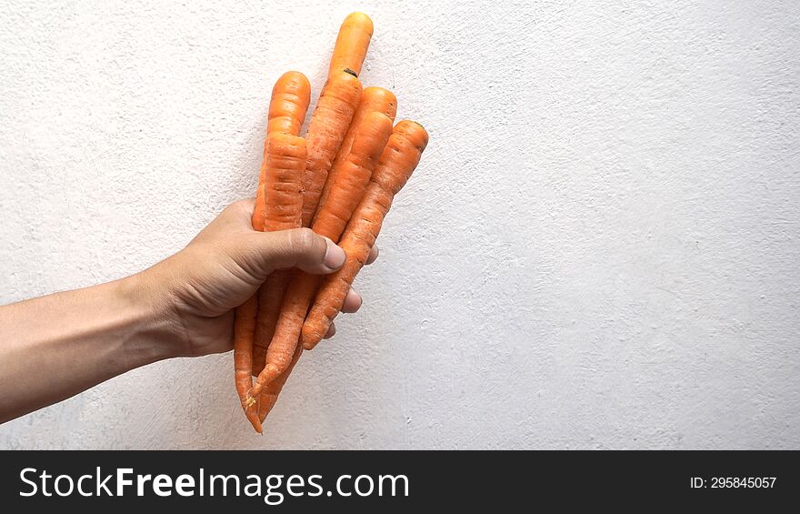 carrot in a man& x27 s hand on a white wall background. Copy space