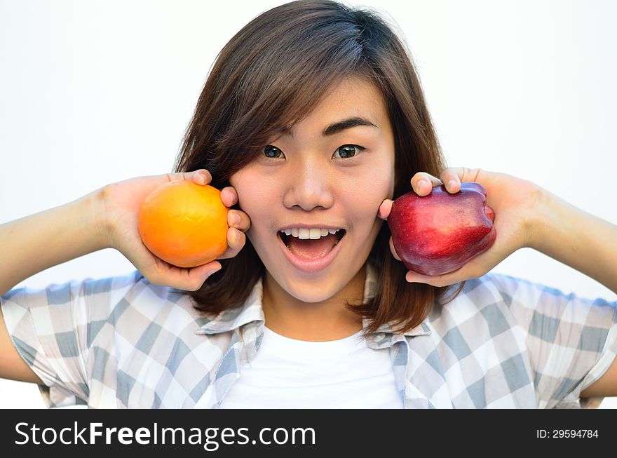 Beautiful asian teenage holding orange and apple fruits near smiling face isolated