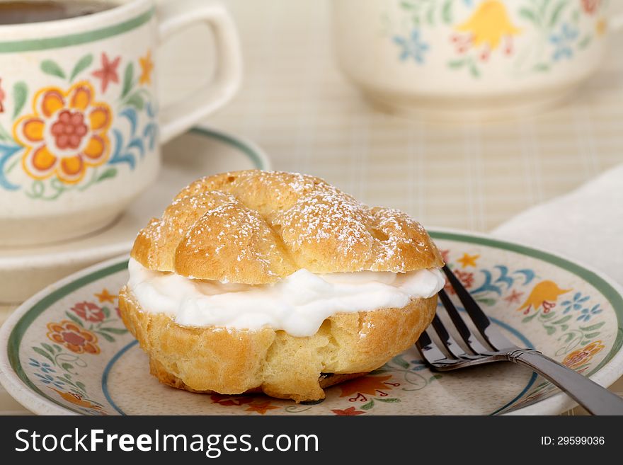 Cream puff with powdered sugar and coffee in background