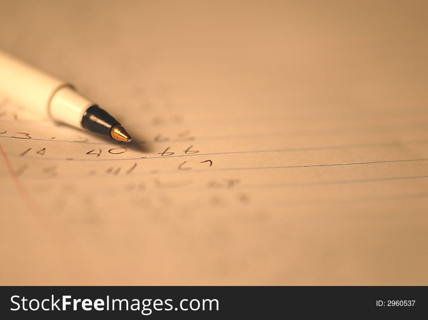 A ballpoint pen lays on a piece of notebook paper with numbers written on it. A ballpoint pen lays on a piece of notebook paper with numbers written on it.