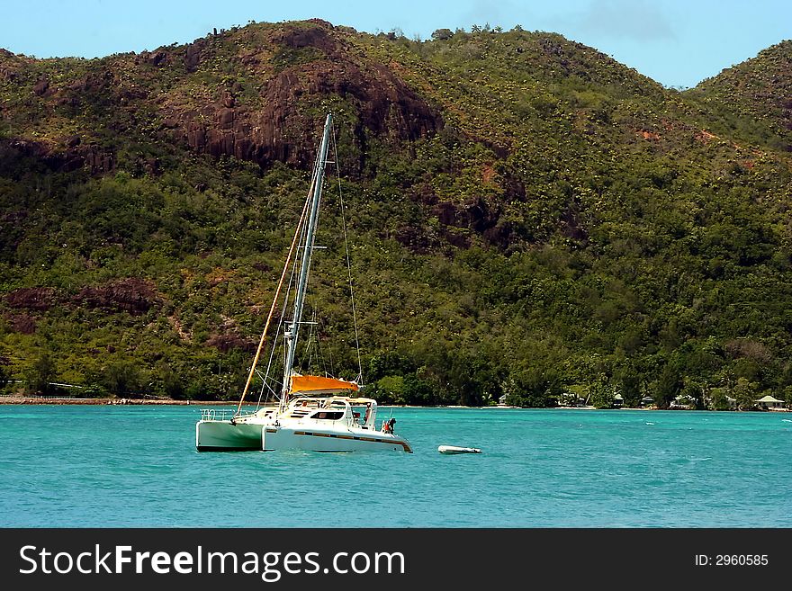 White yacht is arriving tjthe tropical harbore. Sea and the mountain of island as the backgraund. Seychelles. White yacht is arriving tjthe tropical harbore. Sea and the mountain of island as the backgraund. Seychelles.