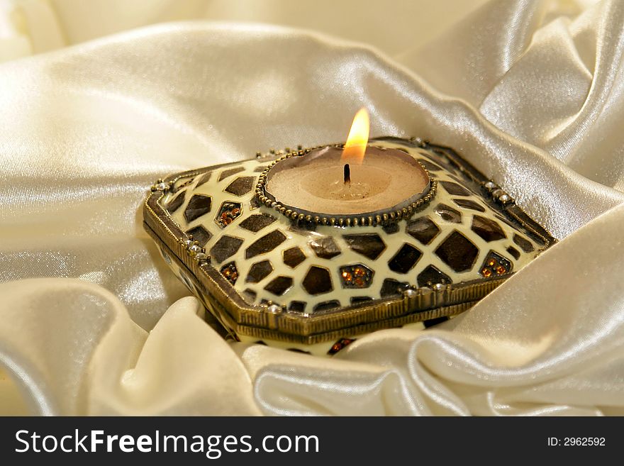Burning candle surrounded by soft folds of glistening satin