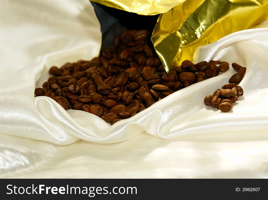 Fresh roasted coffee beans pouring out of bag on satin fabric. Fresh roasted coffee beans pouring out of bag on satin fabric