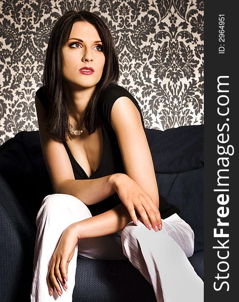 A portrait of beautiful brunette wearing black undershirt and white trousers on patterned background. A portrait of beautiful brunette wearing black undershirt and white trousers on patterned background