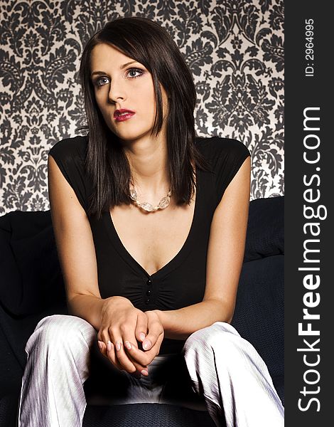 A portrait of beautiful brunette wearing black undershirt and white trousers on patterned background. A portrait of beautiful brunette wearing black undershirt and white trousers on patterned background