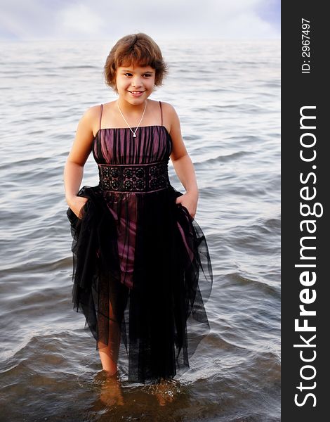 Full-body portrait of an elementary girl in formalwear holding up her skirt while standing in lake water. Full-body portrait of an elementary girl in formalwear holding up her skirt while standing in lake water.