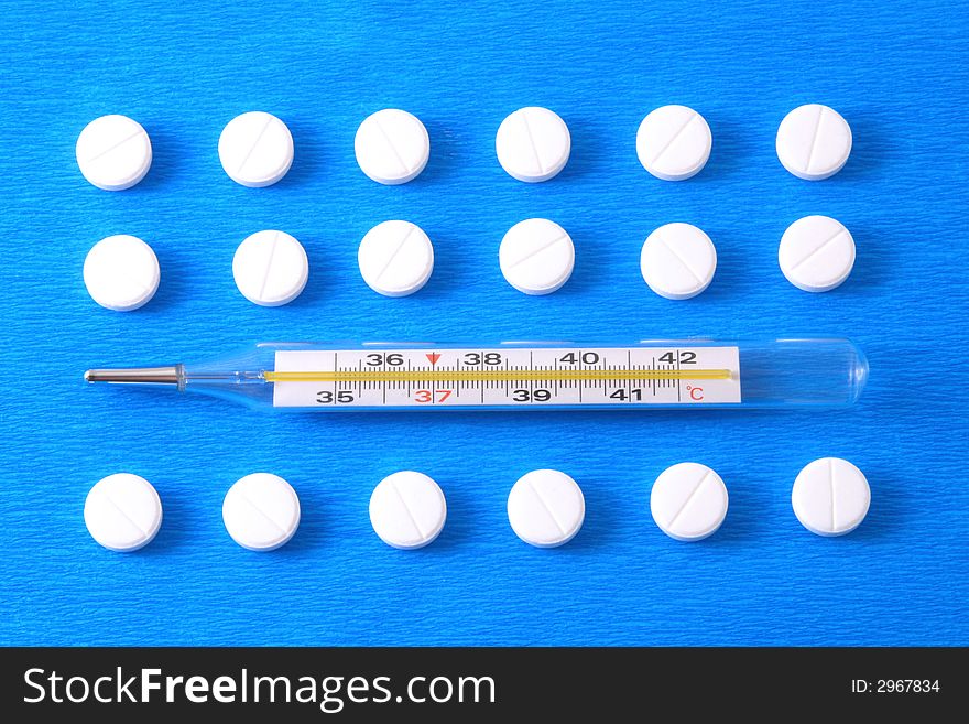 Pills and thermometer on a blue background