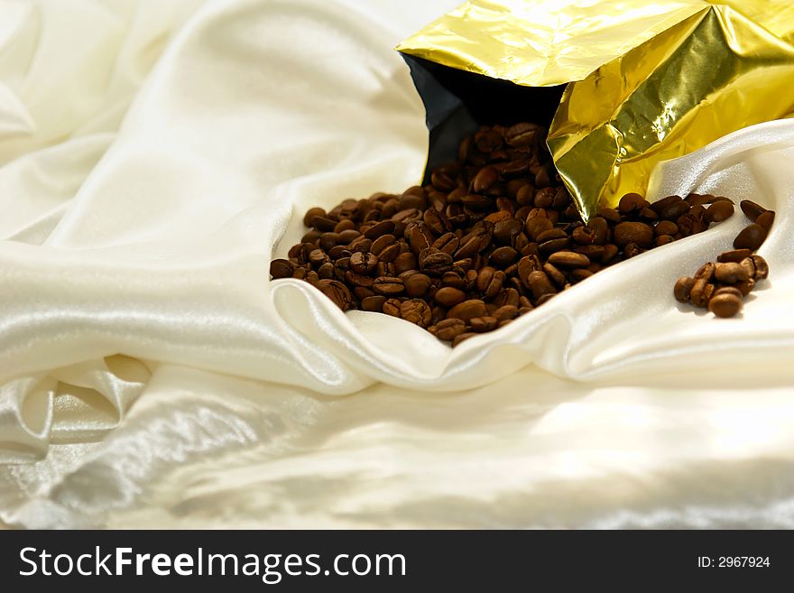 Fresh roasted coffee beans pouring out of bag on satin fabric. Fresh roasted coffee beans pouring out of bag on satin fabric