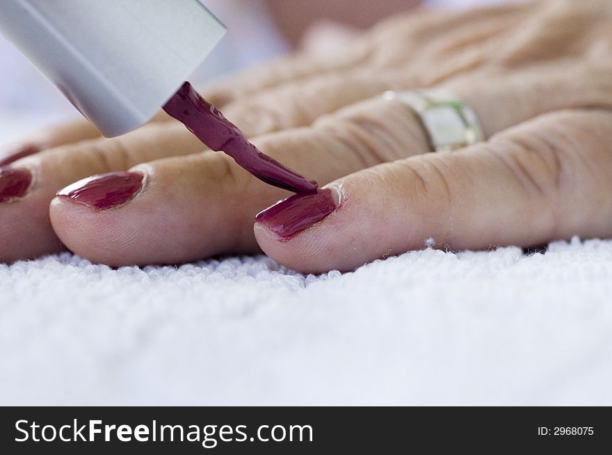 Elderly lady applies dark pink nailpolish to her fingernails. Elderly lady applies dark pink nailpolish to her fingernails