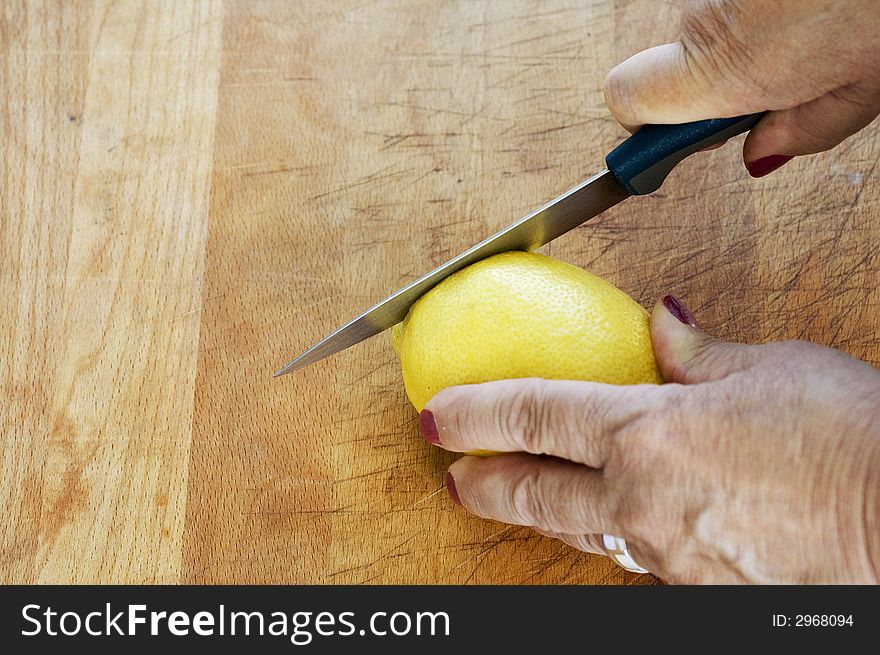 Hands of an elderly lady slice a lemon on a wooden board. Hands of an elderly lady slice a lemon on a wooden board