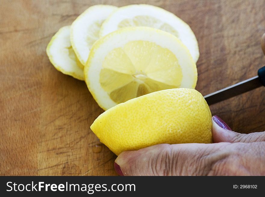 Hands of an elderly lady slice a lemon on a wooden board. Hands of an elderly lady slice a lemon on a wooden board