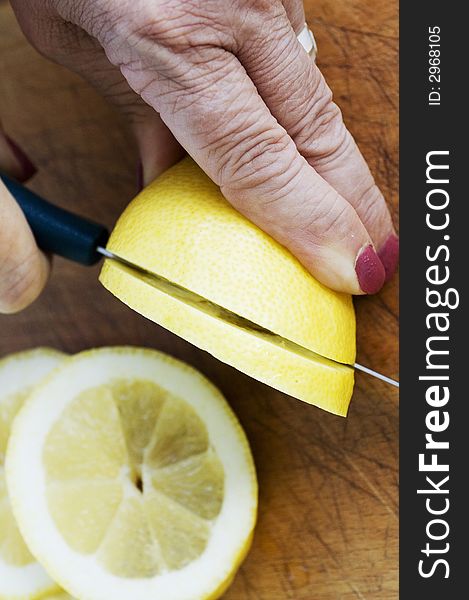 Hands of an elderly lady slice a lemon on a wooden board. Hands of an elderly lady slice a lemon on a wooden board