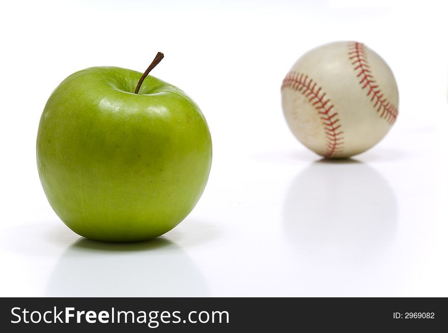 Green granny smith apple and a baseball on white background, symbols of summertime in America