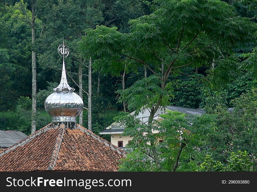 Image Of The Tile Roof Of A Small Mosque, With A Small Aluminum Dome On Top, In The Middle Of Green Forest Trees.