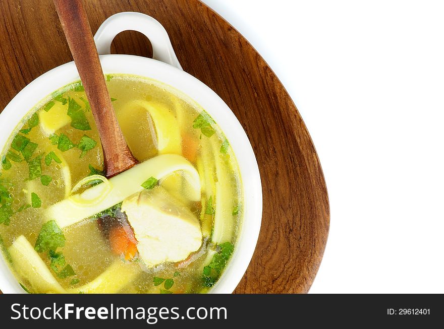 Chicken Noodle Soup with Parsley and Carrot in White Bowl with Wooden Spoon on Wooden Plate. Top View