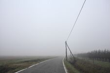 Road Bordered By A Trench And A Power Line Next To Fields On A Foggy Day In The Italian Countryside Royalty Free Stock Images