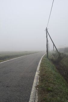Road Bordered By A Trench And A Power Line Next To Fields On A Foggy Day In The Italian Countryside Royalty Free Stock Photography