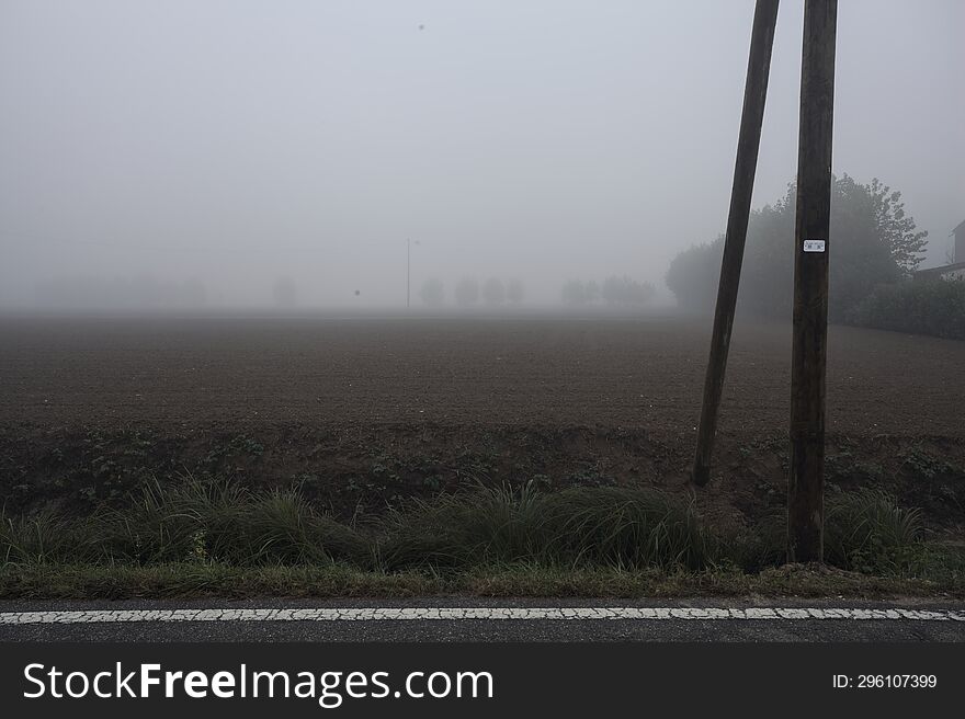 Ploughed Field Bordered By Trees On A Foggy Day In The Italian Countryside Seen From Behind A Trench