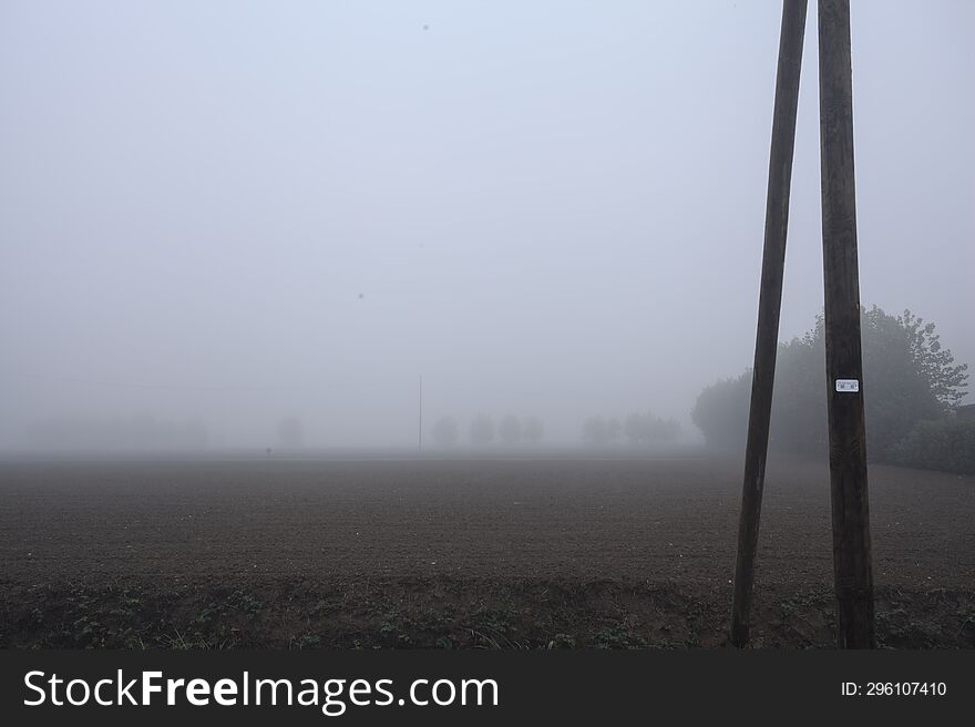 Ploughed field bordered by trees on a foggy day in the italian countryside seen from behind a trench