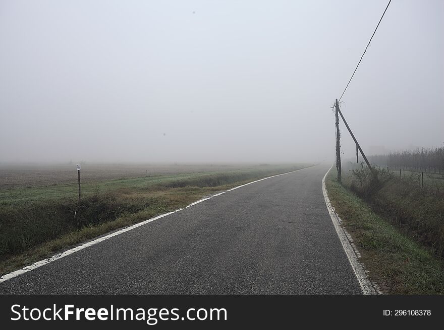 Road Bordered By A Trench And A Power Line Next To Fields On A Foggy Day In The Italian Countryside