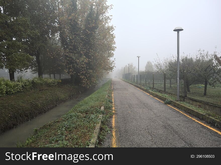 Bike lane on a foggy day next to a trench with water on a foggy day in the italian countryside