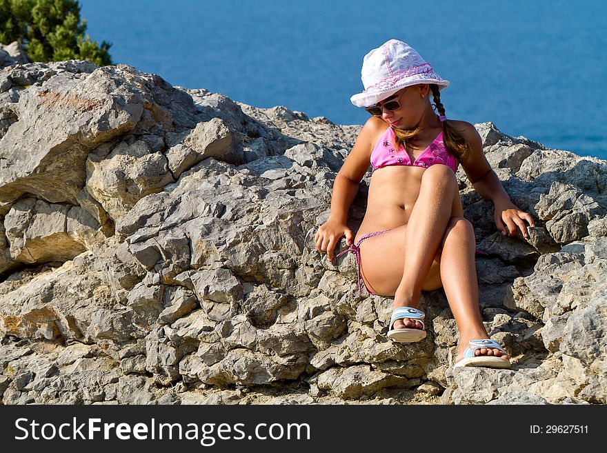 Girl 8 years with white hat and glasses sitting on the rocks by the sea. Girl 8 years with white hat and glasses sitting on the rocks by the sea