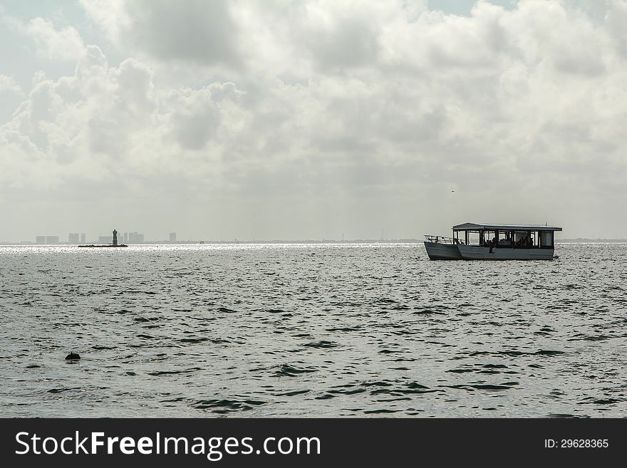 The sun is reflecting off the water and the light house while a boat floats on by off of Isla Mujeres, Mexico. With Cancun in the background. The sun is reflecting off the water and the light house while a boat floats on by off of Isla Mujeres, Mexico. With Cancun in the background.