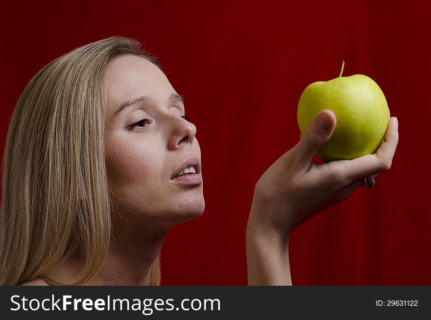 Young blonde holding an apple on red background