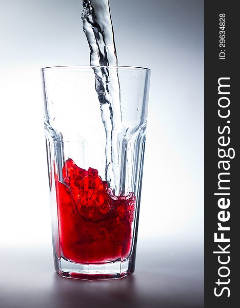 Water pouring into a glass with red juice. Water pouring into a glass with red juice