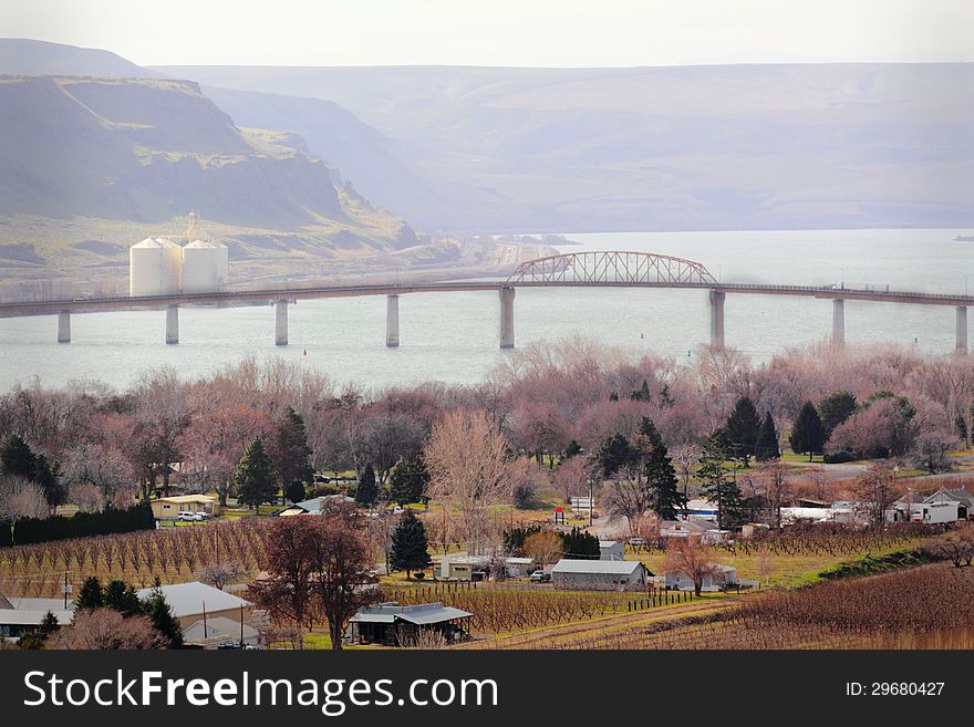 View of a groomed peaceful riverside neighborhood community in winter with buildings, barren trees, bridge over river, distant hills and a grain elevator. View of a groomed peaceful riverside neighborhood community in winter with buildings, barren trees, bridge over river, distant hills and a grain elevator.