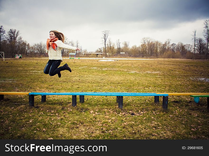 Teen Girl Wearing Orange Scarf Jumping Over Bench In Windy Day. Teen Girl Wearing Orange Scarf Jumping Over Bench In Windy Day